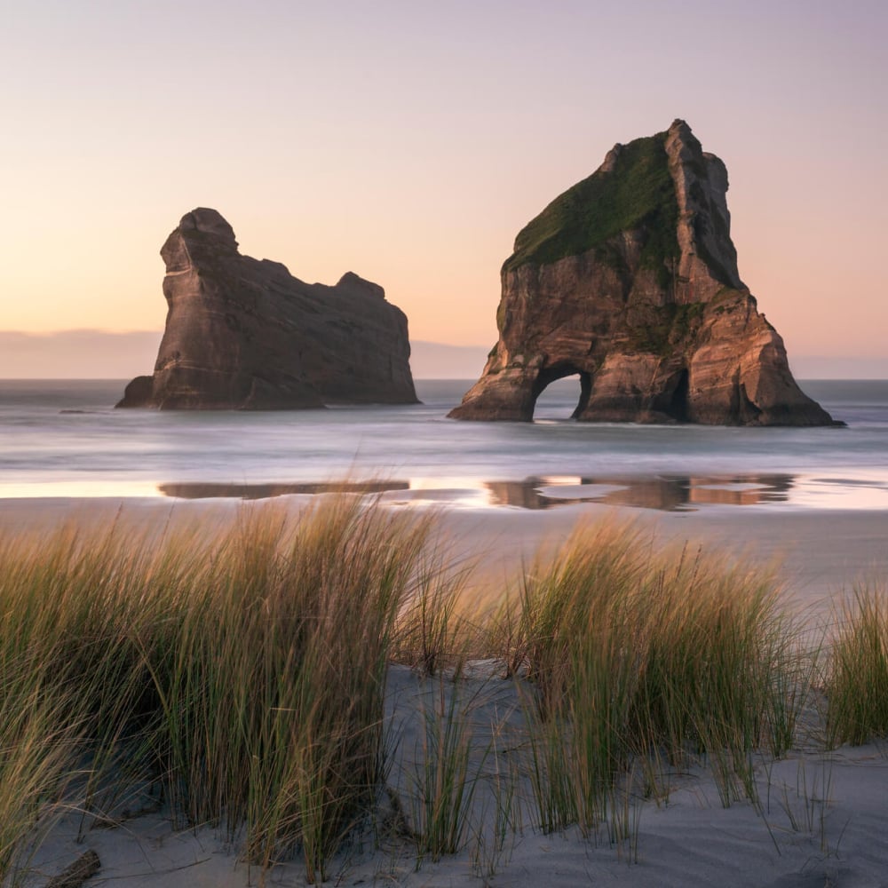 Wharariki Beach is a wild, windswept stretch of sand framed by towering rock arches and rolling dunes.